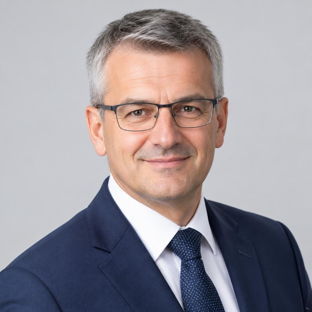 Studio portrait of a Central European man with grey hair and glasses in a navy suit